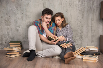 Obraz premium Photo of young couple sitting on the floor and reading a book