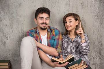 Photo of young smiling couple sitting on the floor with books