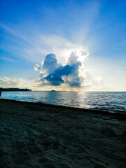 El sol iluminando desde atrás a nubes sobre el mar en una bella playa por la mañana+nubles, resplandor, sol, playa, mañana, azul
