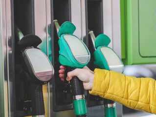 The hand of a young Caucasian man in a yellow jacket takes a filling gun at a gas station