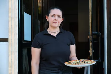 Möbelaufkleber Latin waitress holding plate with pizza at the restaurant door. Pizzeria. © Ladanifer