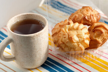 Cream puffs cakes or profiterole filled with whipped cream in plastic box. eclairs and a ceramic cup of tea. Traditional french tasty dessert.