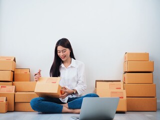 Cheerful Asian people checking order online on laptop,Asian woman packing parcel at home.