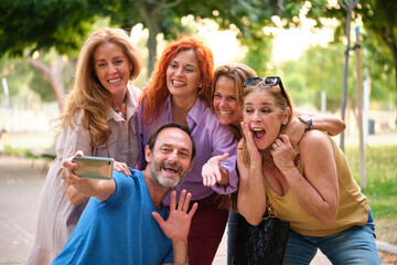 Portrait of five mature adults taking a selfie and having fun in a park.