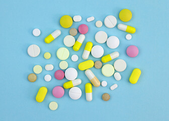 Pills of different sizes and colors on a blue background. Capsules and tablets colored top view. Dietary supplements of various types.
