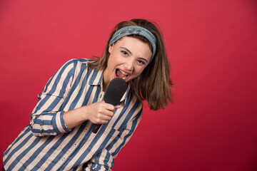 Young funny girl sings using black hairbrush on red background