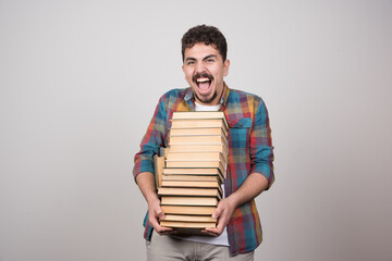 Exhausted student with pile of books screaming on gray background