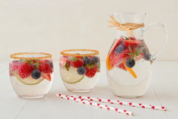 Homemade lemonade with fresh summer berries in pitcher and 2 glasses on white wooden table, no people, low angle view.