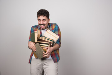 Young man holding a lot of books on a gray wall