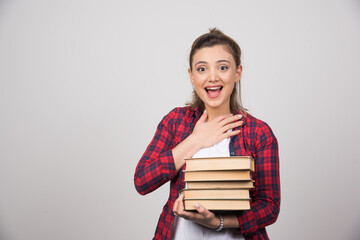 A happy woman carrying a stack of books on a gray wall