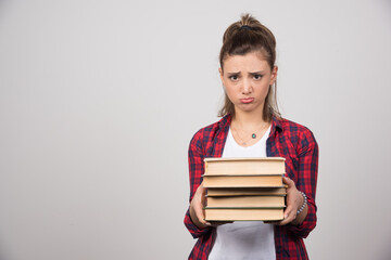 An upset woman showing a stack of books on a gray wall
