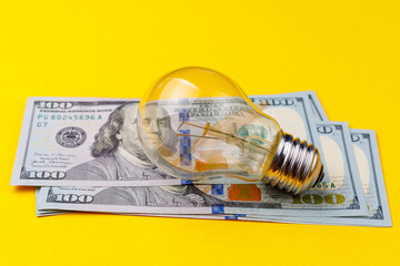 Classic electric light bulb on a blurred background of dollar cash bills or banknotes
