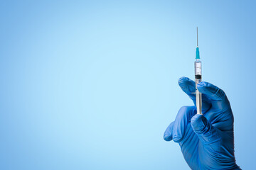 Doctors hand in surgical gloves holds a syringe on classic symbolic blue background - obrazy, fototapety, plakaty