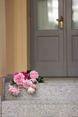Fototapeta na wymiar Bouquet of pink gardening peonies lies on steps near the old grey wooden door.