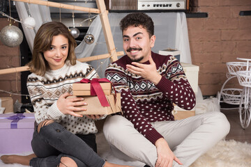 Young couple sitting with Christmas presents near festive silver balls