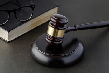 Brown golden wooden gavel of judge on dark table with black book and glasses.