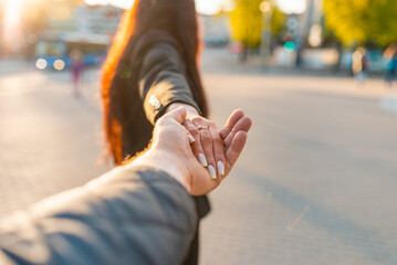Happy brunette girl turn away face holding boyfriend's hand on a street at sunset on a warm spring,summer evening.Follow-me concept.Selective focus.
