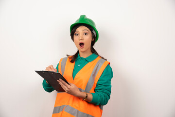 Shocked female industrial engineer in uniform with clipboard on white background