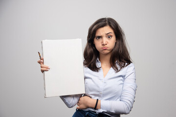 Naklejka premium Tired woman showing empty canvas and paintbrush on gray background
