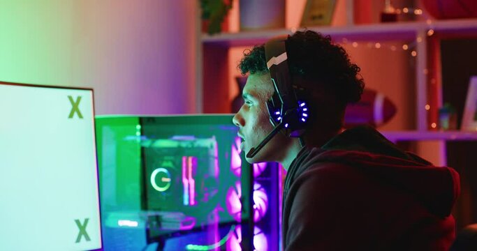 Young gamer playing online video games on a computer monitor with green screen copy space. Streamer using a headset with a microphone and a controller accessing an online, open world multiplayer game