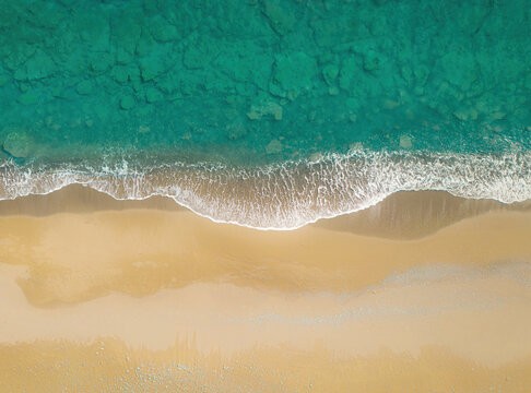 Green sea waves breaking on a golden sand shore. Top view directly above, natural background