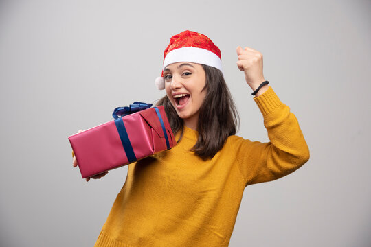 Brunette woman in Santa hat showing her fist and holding gift box