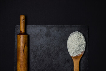Wooden spoon with flour and a rolling pin on a black background. The concept of baking and confectionery.