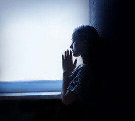 Young girl prays at the window