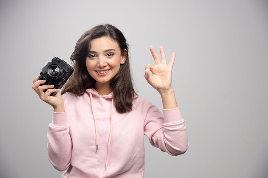 Female photographer holding camera and making ok sign
