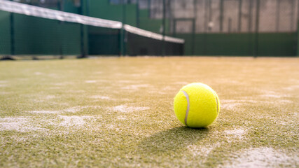 Yellow ball on floor behind paddle net in green court outdoors. Padel tennis