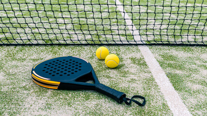 Yellow balls on grass turf near padel tennis racket behind net in green court