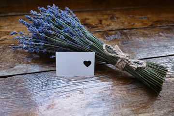 Mockup of a greeting card or card for wishes and a bouquet of lavender on a wooden background. Greeting card. Bouquet of fragrant lavender. Place for text
