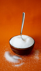 white sugar in a brown bowl with a spoon on orange background with space for text in vertical format