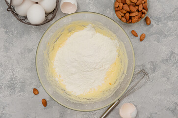Recipe step by step. The process of making Italian cantucini cookies. Whipped eggs with sugar, butter, flour and baking powder in a bowl on a gray concrete background. Top view.