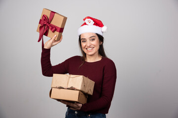 Young woman in Santa hat showing Christmas presents on gray background