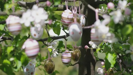 Decor eggs on flowering apple branches on a tree in a garden or park. Pink and gold ornament from stripes and spots.