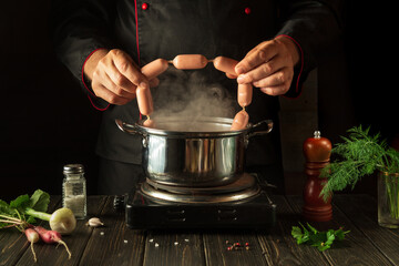 The chef puts the Viennese sausages into the pan. Working environment in the kitchen of a restaurant or cafe. Preparing breakfast or lunch