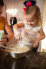 Imagem de mãe e filha brincando enquanto cozinham um bolo. Mulher loira brincando com sua filha na cozinha. Receita de doce feita em família.