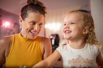 Imagem de mãe e filha brincando enquanto cozinham um bolo. Mulher loira brincando com sua filha na cozinha. Receita de doce feita em família.
