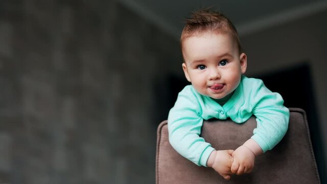 Playful beautiful kid with funny hair standing on the chair. Lovely toddler showing tongue and smiling. Low angle view.