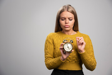 Blonde girl holds an alarm clock and setting up a time