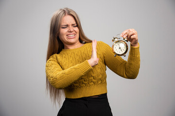 Blonde girl holds an alarm clock and gets disturbed of the loud voice