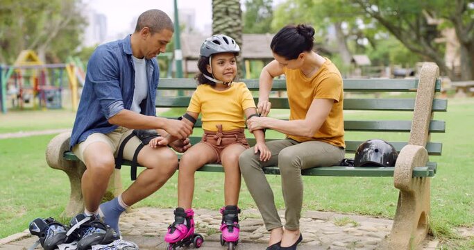 Caring parents making sure their daughter is safe and protected while rollerskating at a public park. Cute little adopted girl wearing protective gear and rollerskates while having fun outdoors