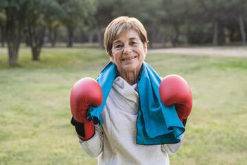 Senior woman smiling on camera after boxing training routine outside at city park - Focus on gloves