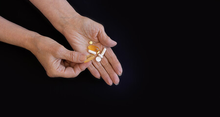 An elderly woman chooses which pill to take, hands on a black background