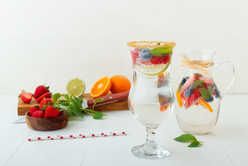Homemade lemonade with fresh summer berries in pitcher and glass on white wooden table, no people, low angle view.
