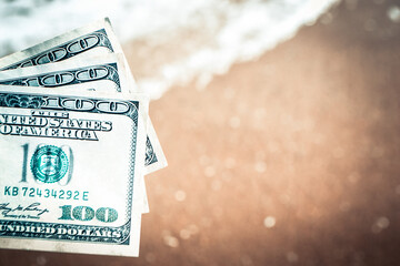 Girl holding money bill of 300 dollars on background of sea ocean waves with white foam and sand wet beach close-up. Hand wave sea ocean money dollars vacation. Concept finance money holiday traveling