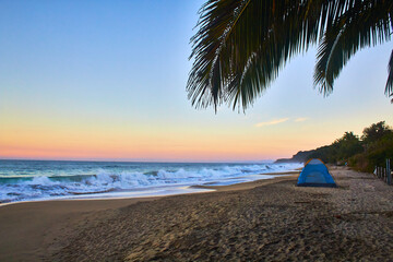 camping tent on the beach at sunrise with sky full of colors and palm tree on first plane in sayulita mexico 