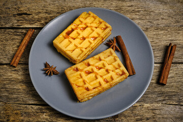 Soft waffles in plate loaded with honey, on wooden table.