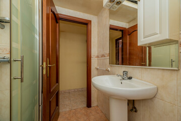 Bathroom with white wood-framed mirror, glass-enclosed shower stall and white porcelain toilets and varnished brown wooden door